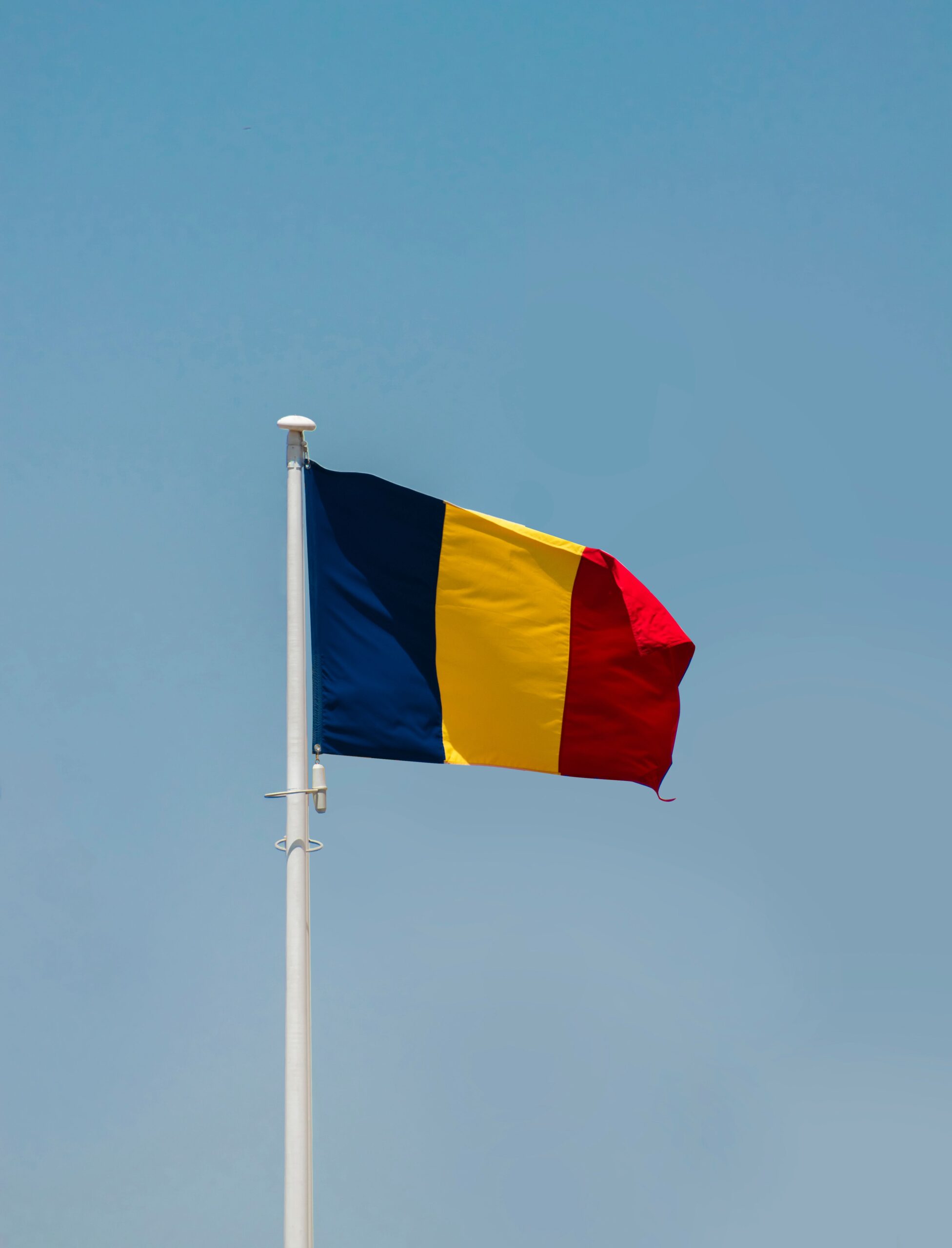 Vibrant Romanian flag flying on a flagpole in Bucharest against a clear sky.